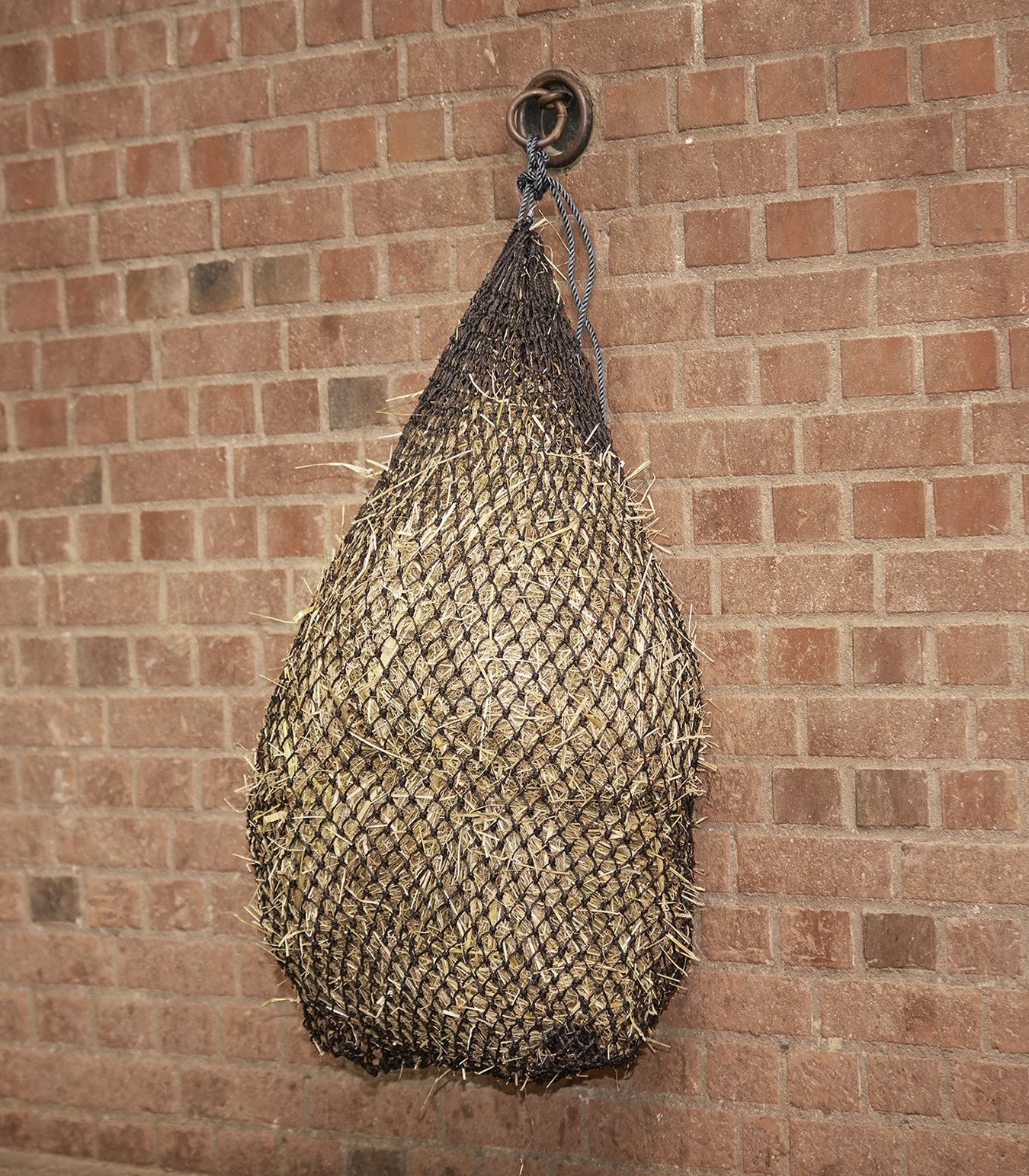 Black Waldhausen large slow feed hay net hanging with hay inside, designed for equine use.